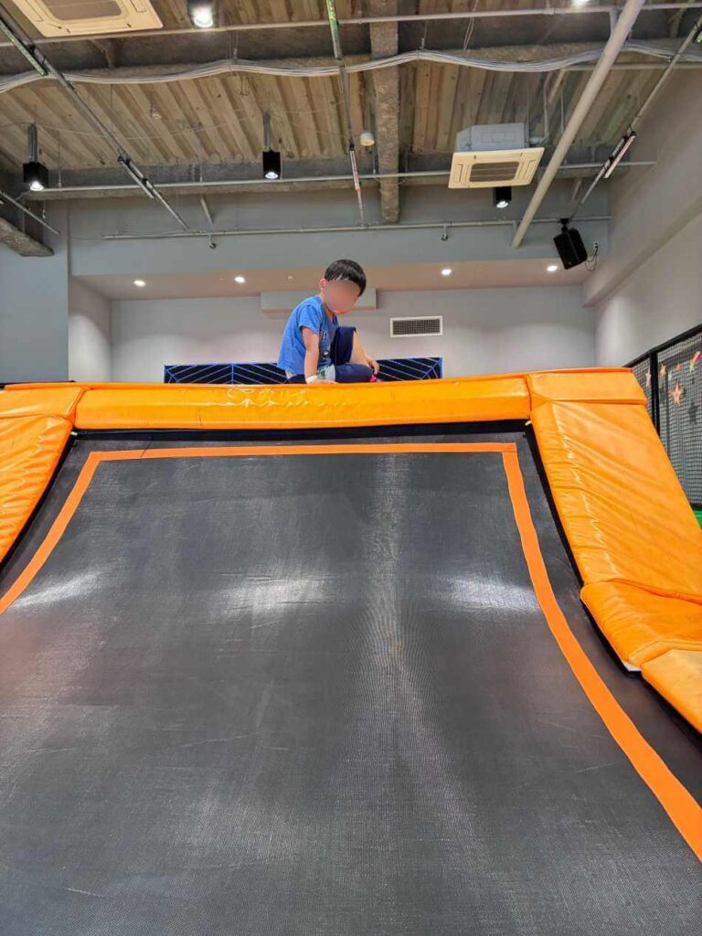 トランポリンの傾斜を登りきって笑顔の子ども